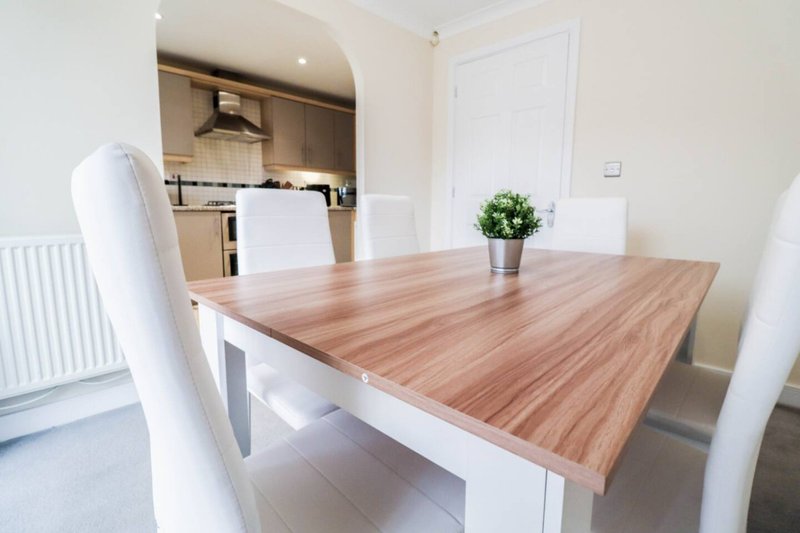 Modern dining table with white chairs, open-plan kitchen and white door visible