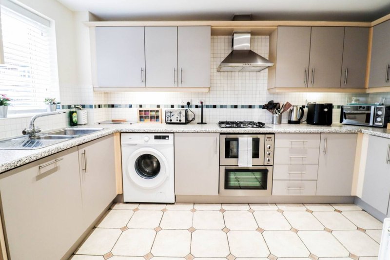 Modern kitchen with cream cabinets, white appliances, granite countertop and tiled flooring