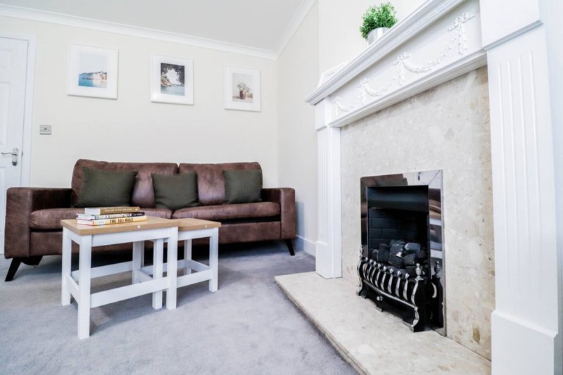 Light living room with brown sofa, white coffee table, fireplace and framed wall art