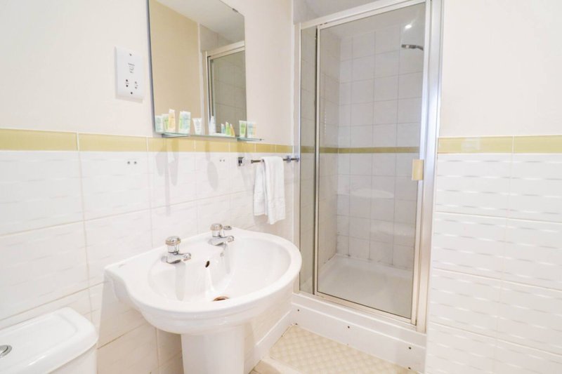 Clean bathroom with pedestal sink, mirror, shower cubicle and white tile walls