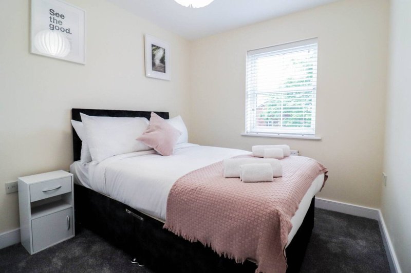 Bedroom with single bed, pink bedding, white pillows, bedside table and window