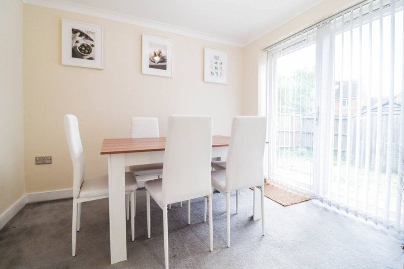 Dining room with white table, four chairs, framed wall art, and large window with blinds