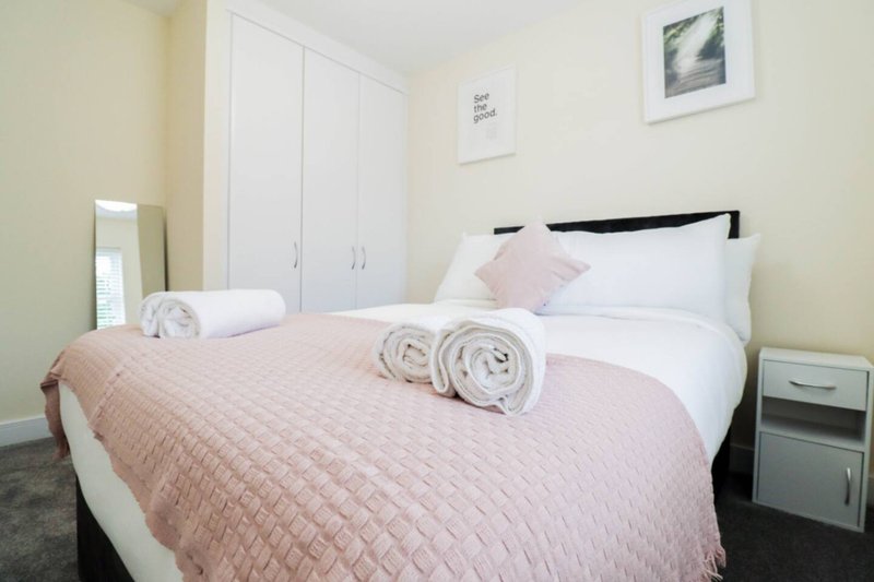 Bright bedroom with double bed, pink bedding, white wardrobe and bedside tables