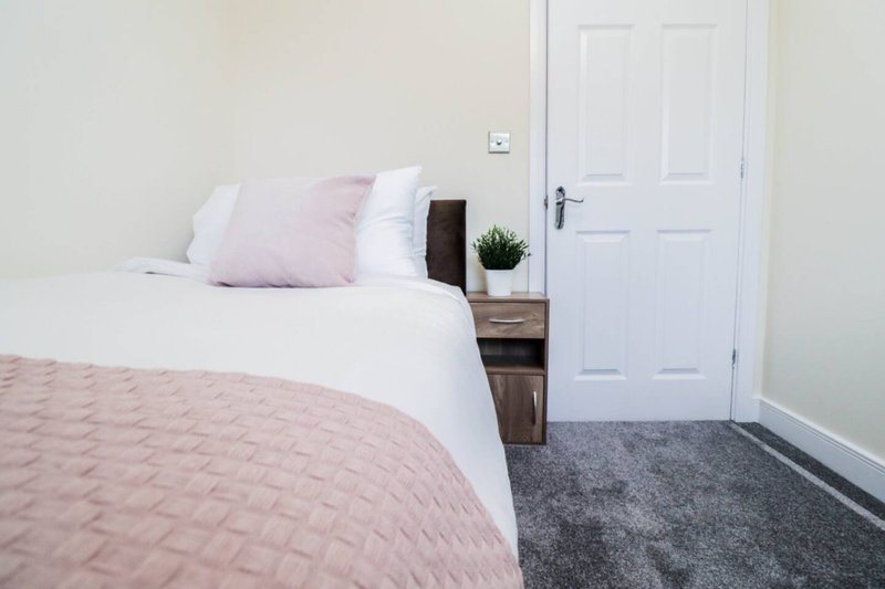Bedroom with double bed, pink quilt, white pillows, wooden nightstand, and white door