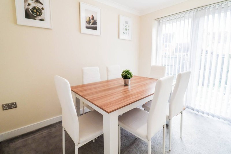 Modern dining room with wooden table, white chairs, framed wall art and glass doors
