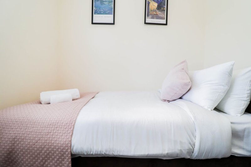 Bedroom with double bed, white pillows, pink throw blanket, and framed wall art
