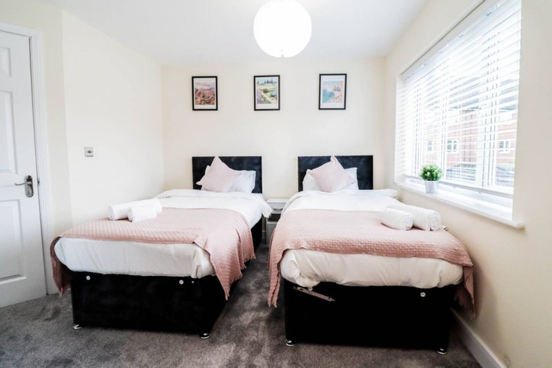 Twin bedroom with two single beds, white pillows, pink throws, and framed artwork on walls