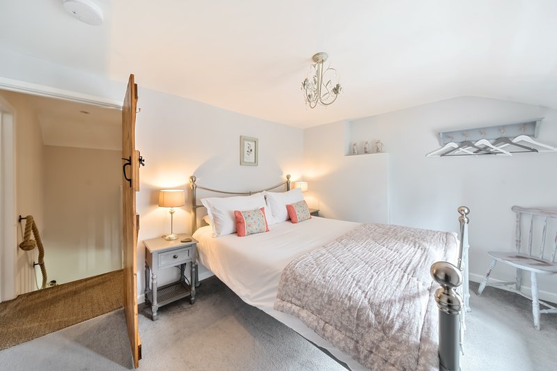 Bright bedroom with double bed, bedside lamps, wooden door and white walls