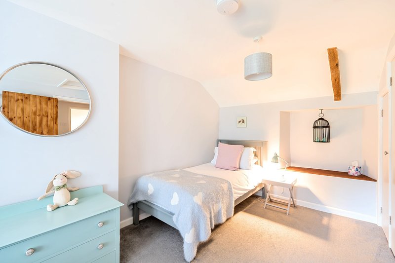 Bright bedroom with single bed, turquoise dresser, round mirror and decorative wall hangings
