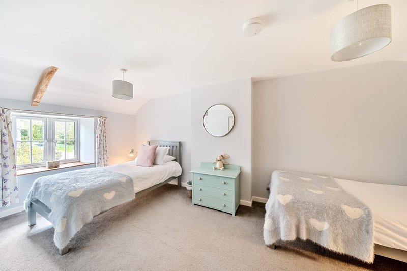 Bright bedroom with two single beds, mint-green nightstand, round mirror and garden view