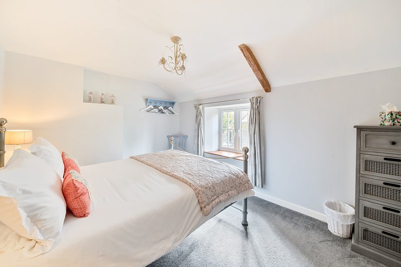 Bright bedroom with double bed, white bedding, coral cushion, wooden beam and window