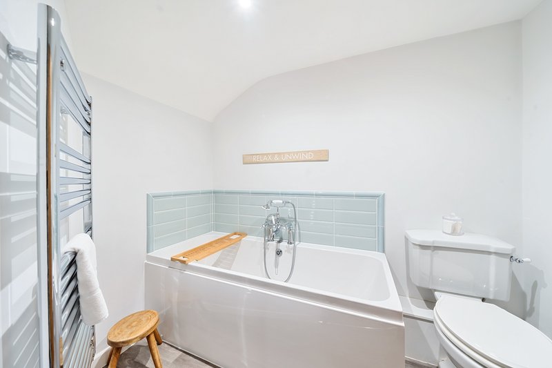 Modern bathroom with white bathtub, wooden stool, tiled surround and toilet