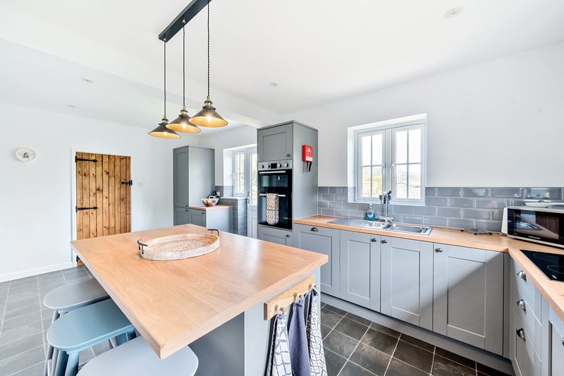Modern kitchen with wooden island, grey cabinetry, pendant lights and dining area