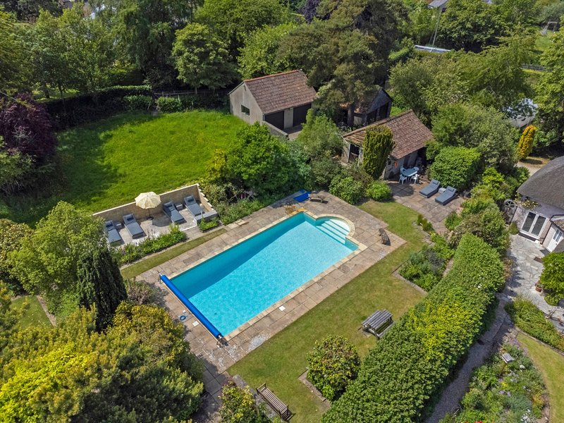 Aerial view of residential property with swimming pool, manicured lawn and surrounding trees