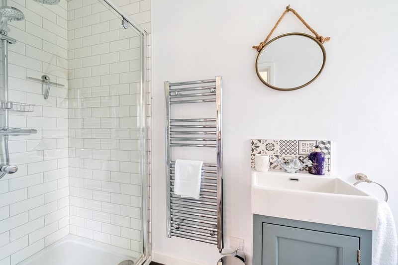 Clean modern bathroom with shower cubicle, heated towel rail, sink and round mirror