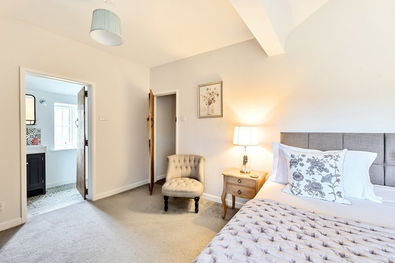 Bright bedroom with double bed, gray headboard, bedside table, lamp, and seating area