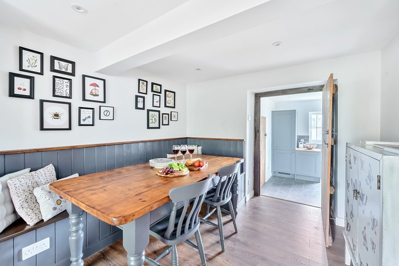 Bright dining area with wooden table, blue bench seating, framed wall art and kitchen access