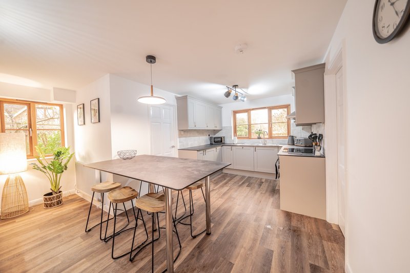 Open-plan kitchen and dining area with wooden flooring, dining table with stools, and modern cabinetry