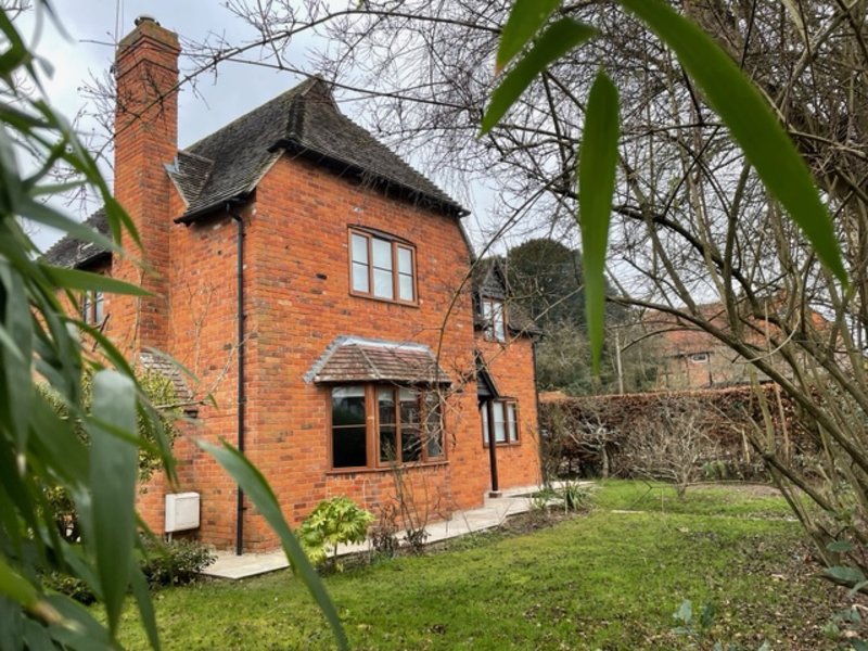 Red brick cottage with chimney, front door, garden, and bare trees