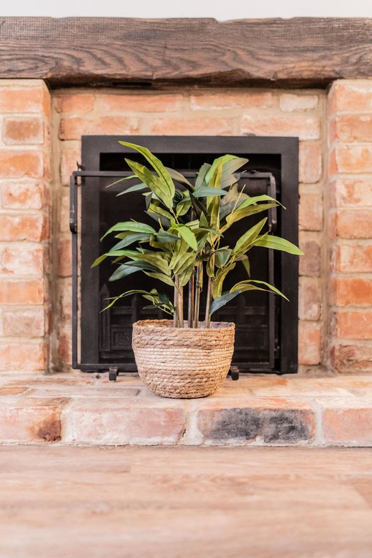 Brick fireplace with black insert and potted green plant in woven basket
