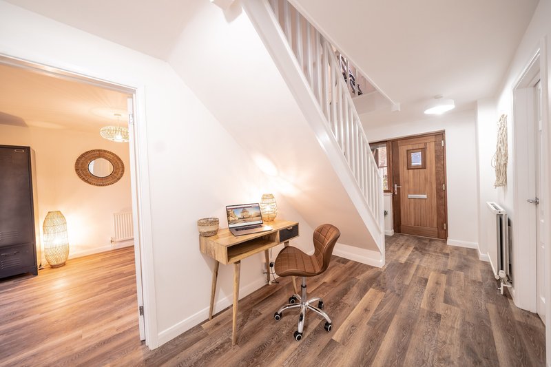 Modern hallway with wooden desk, office chair, staircase and open-plan living area
