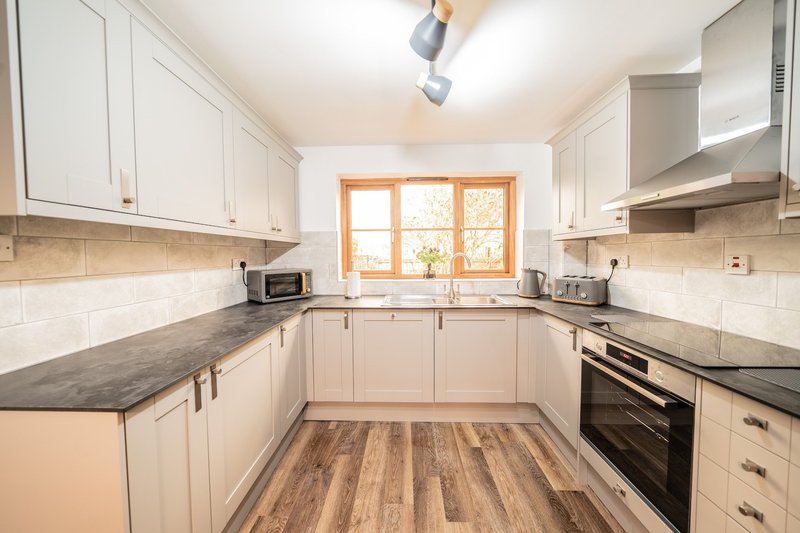 Modern kitchen with white cabinetry, black countertops, wooden flooring and window