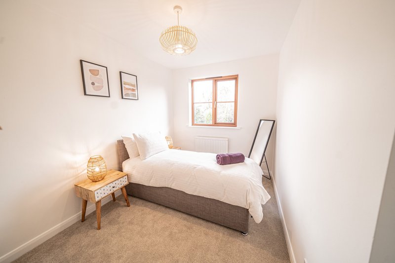 Bright bedroom with double bed, wooden nightstand, pendant light, framed wall art and window