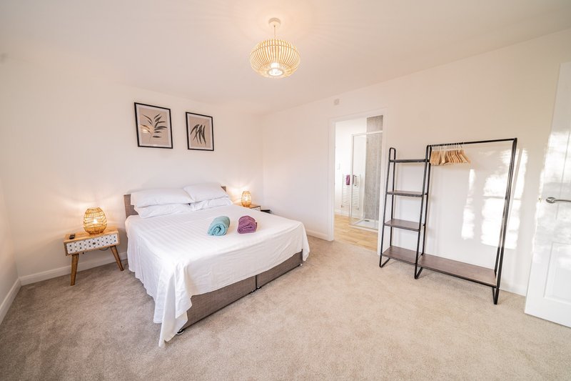 Bright bedroom with white bedding, wooden nightstand, pendant light fixture and ladder shelving