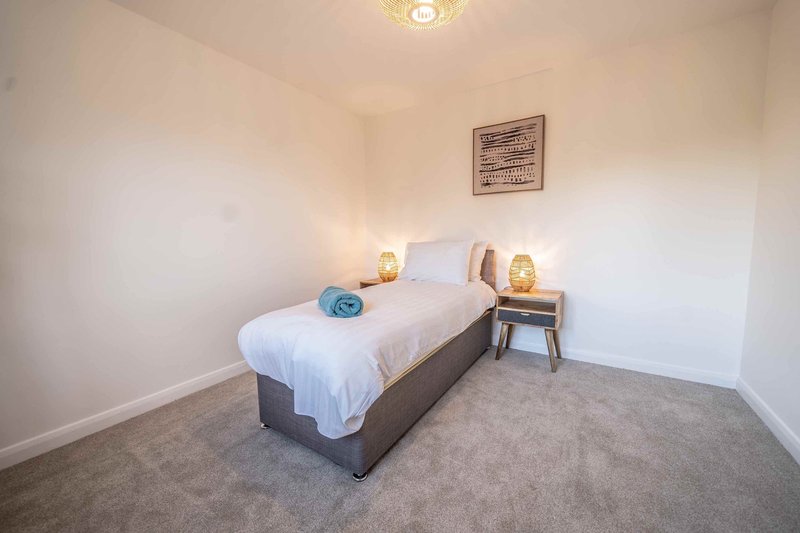 Bedroom with single bed, white bedding, bedside table with lamp, and framed wall art