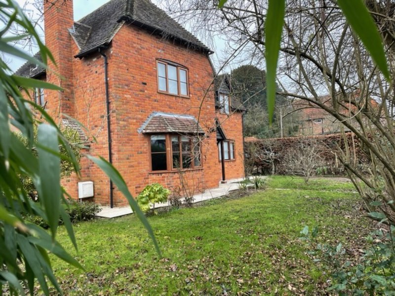 Red brick detached house with garden, bare trees, and green lawn frontage
