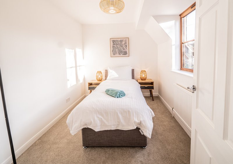 Bright bedroom with single bed, white bedding, wooden bedside tables and windows