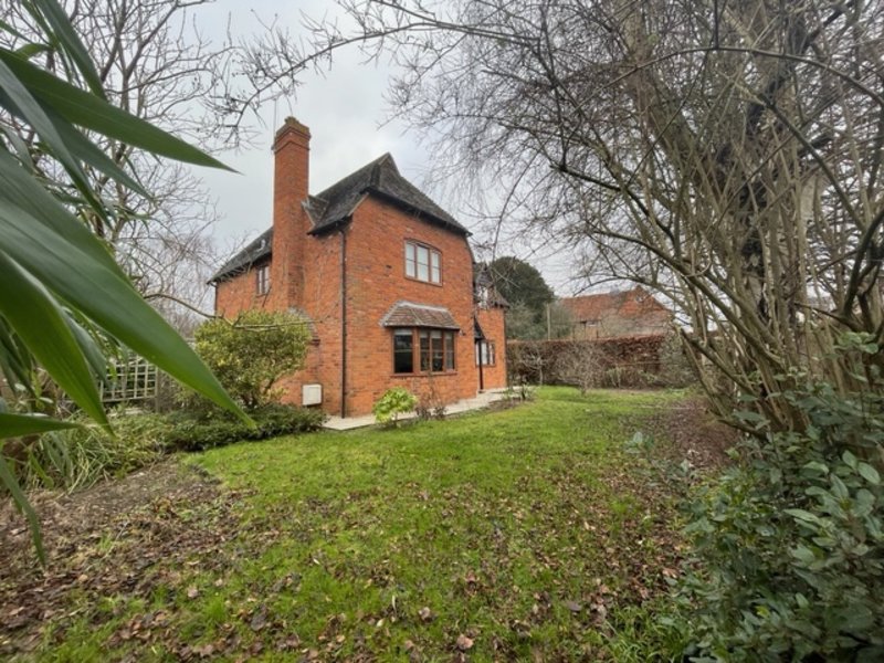 Red brick house with chimney, lawn, and bare trees in winter garden setting