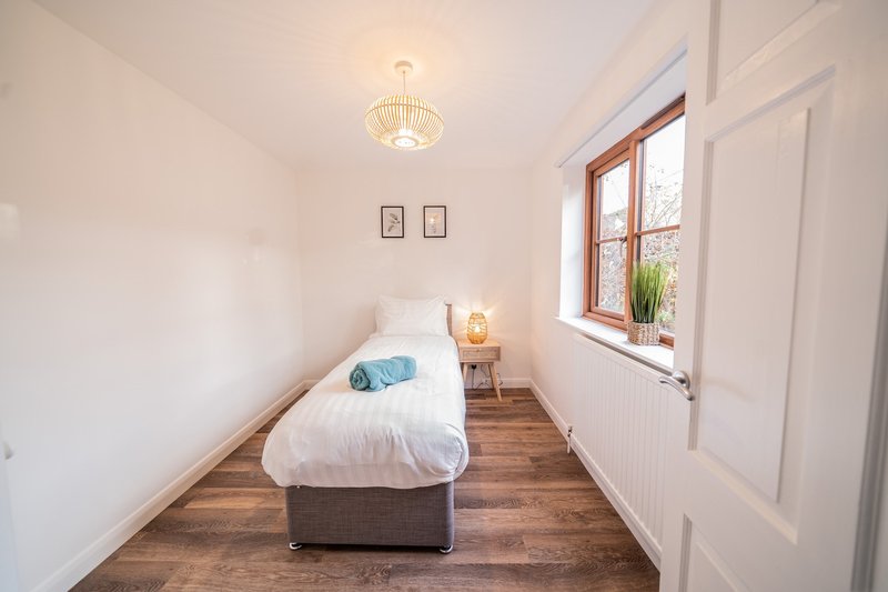 Narrow bedroom with single bed, wooden floor, pendant light and window