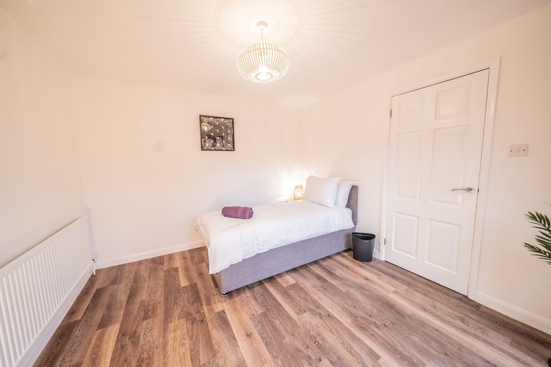Bedroom with single bed, wooden laminate floor, white walls and ceiling light
