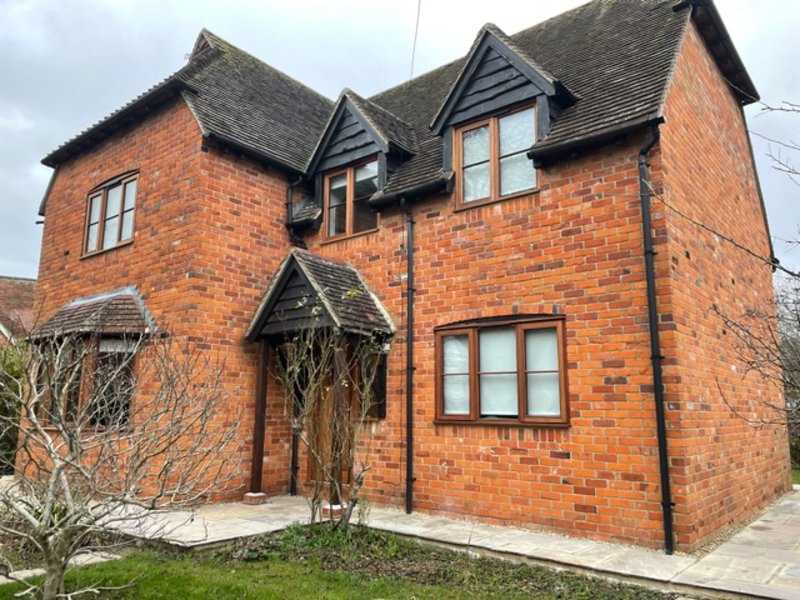 Red brick two-story house with dark roof, arched entrance, and front garden with bare climbing vines