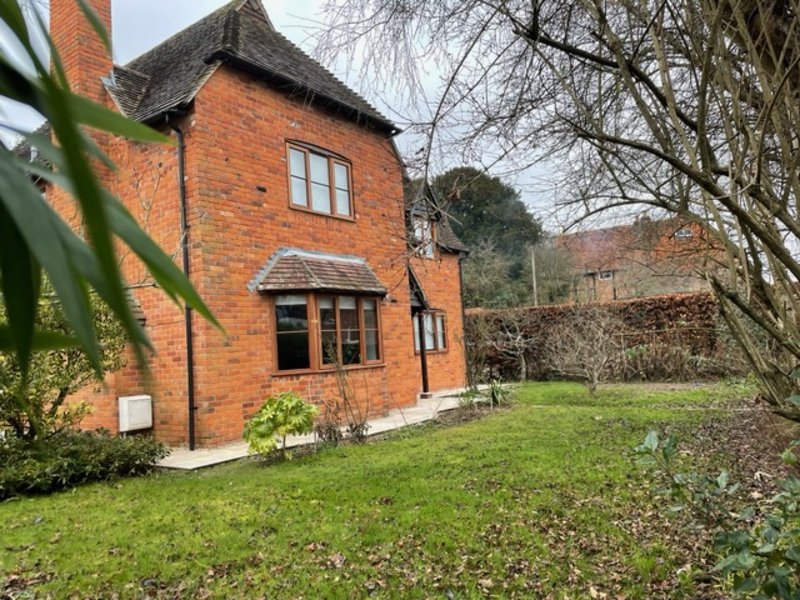 Red brick cottage exterior with green lawn, garden, bare trees and countryside surroundings