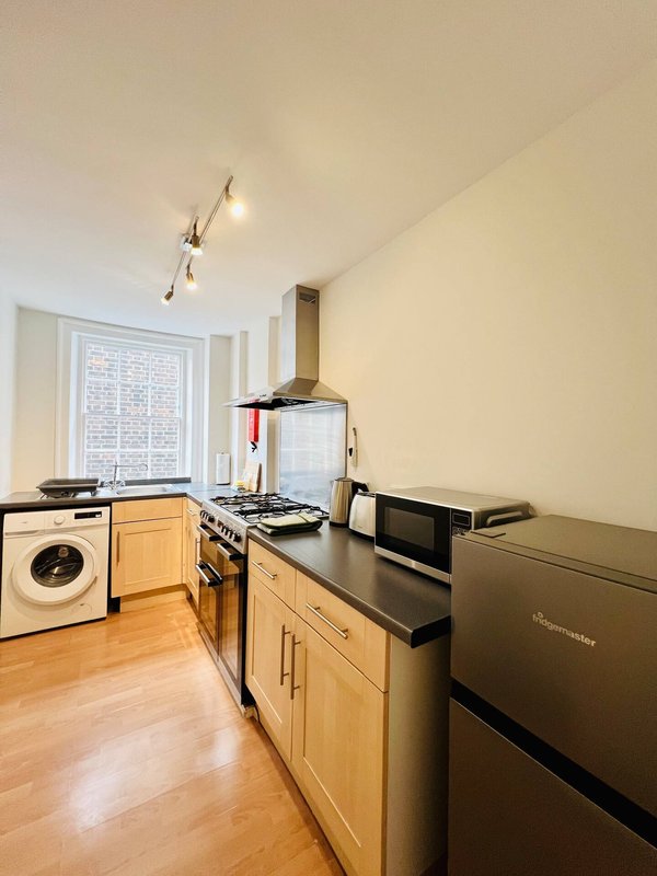 Kitchen with wooden cabinets, gas range, washing machine, and window overlooking street