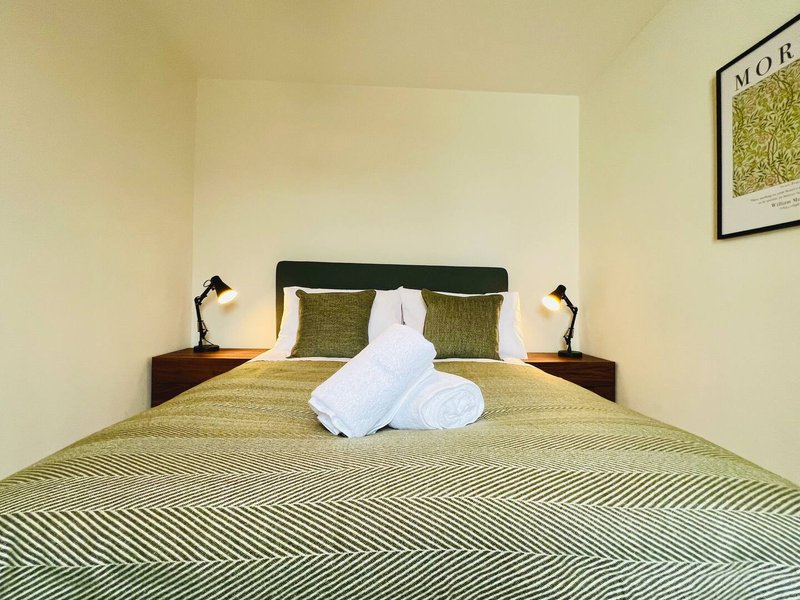 Bedroom with double bed, white towels, green bedding, wooden side tables and wall art