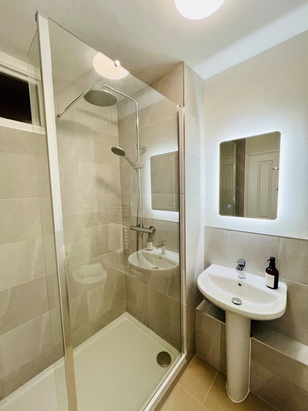Modern bathroom with walk-in shower, pedestal sink, and illuminated mirror