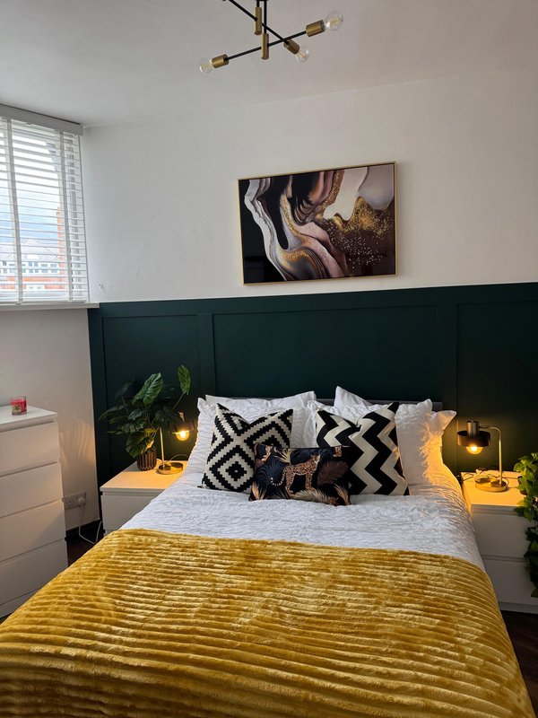 Modern bedroom with dark green headboard, yellow bedding, patterned cushions and wall art