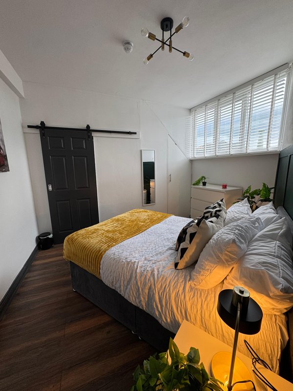 Modern bedroom with double bed, yellow throw, black sliding door, and ceiling light fixture