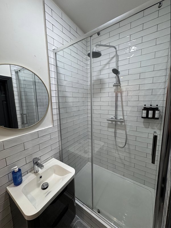 Modern bathroom with white subway tile, glass shower enclosure, round mirror and white sink