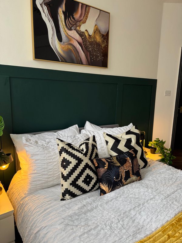 Bedroom with green headboard, white bedding, patterned cushions and wall art