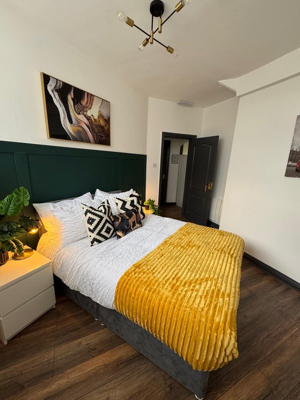 Modern bedroom with double bed, green headboard, yellow throw blanket and patterned cushions