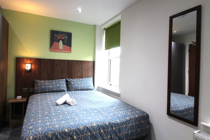 Modern bedroom with double bed, geometric blue bedding, lime green accent wall, and floor mirror