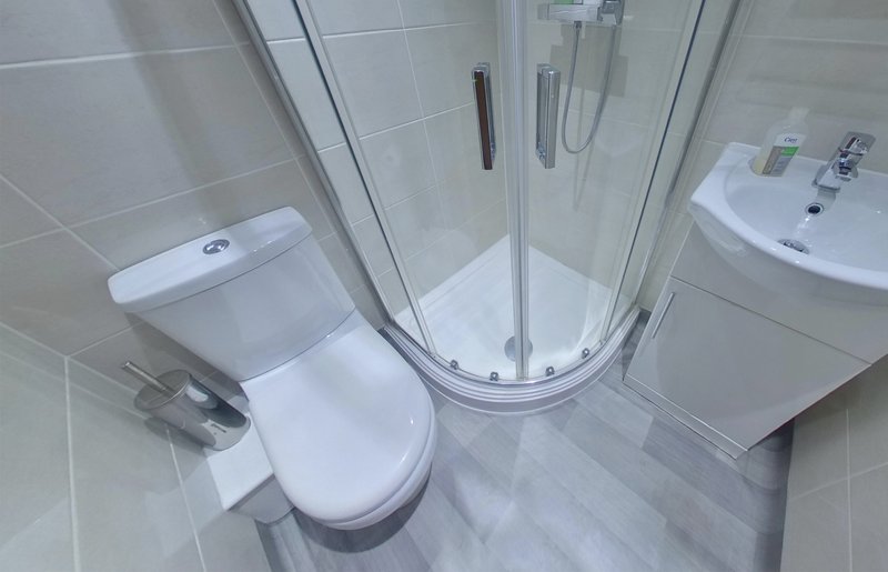 Clean modern bathroom with toilet, curved shower enclosure, and white sink