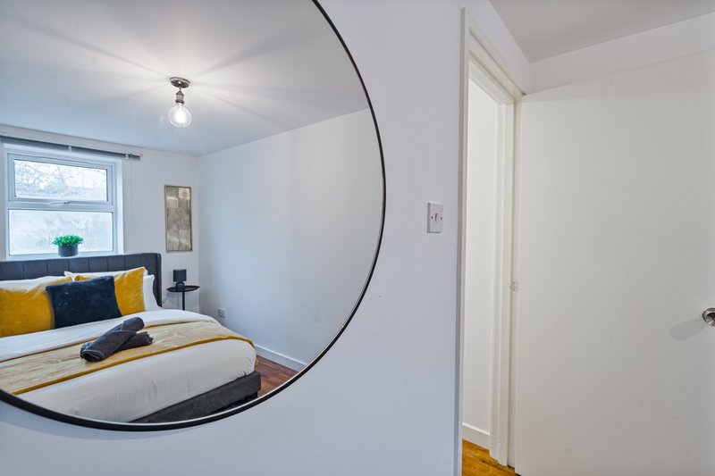 Bright bedroom with double bed, round mirror, window, and wooden flooring