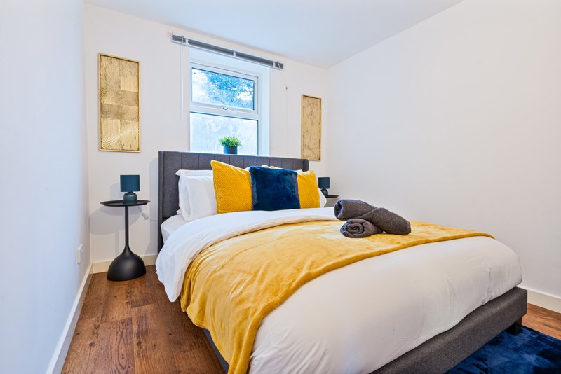 Bedroom with double bed, yellow duvet, decorative pillows, wooden floor and window