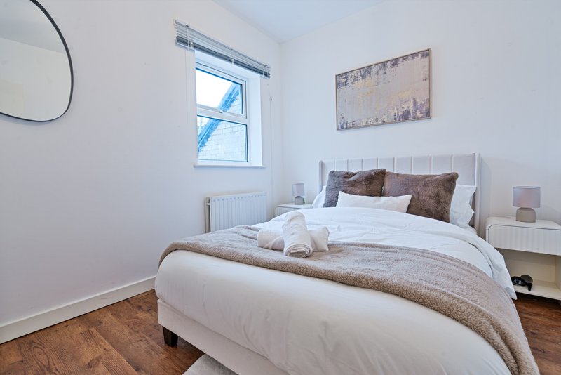 Bright bedroom with double bed, white bedding, brown cushions, wooden floor and window