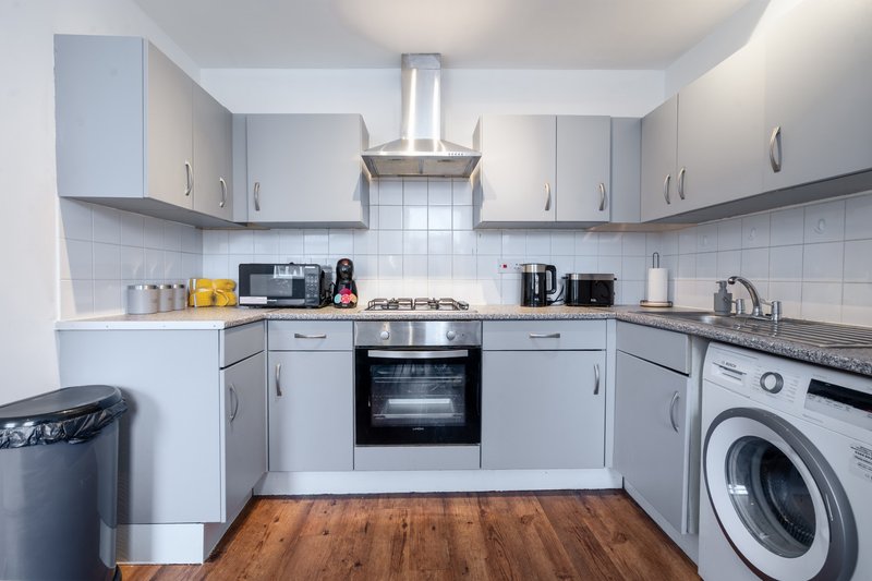 Modern kitchen with white cabinets, built-in oven, gas hob, washing machine and wooden flooring